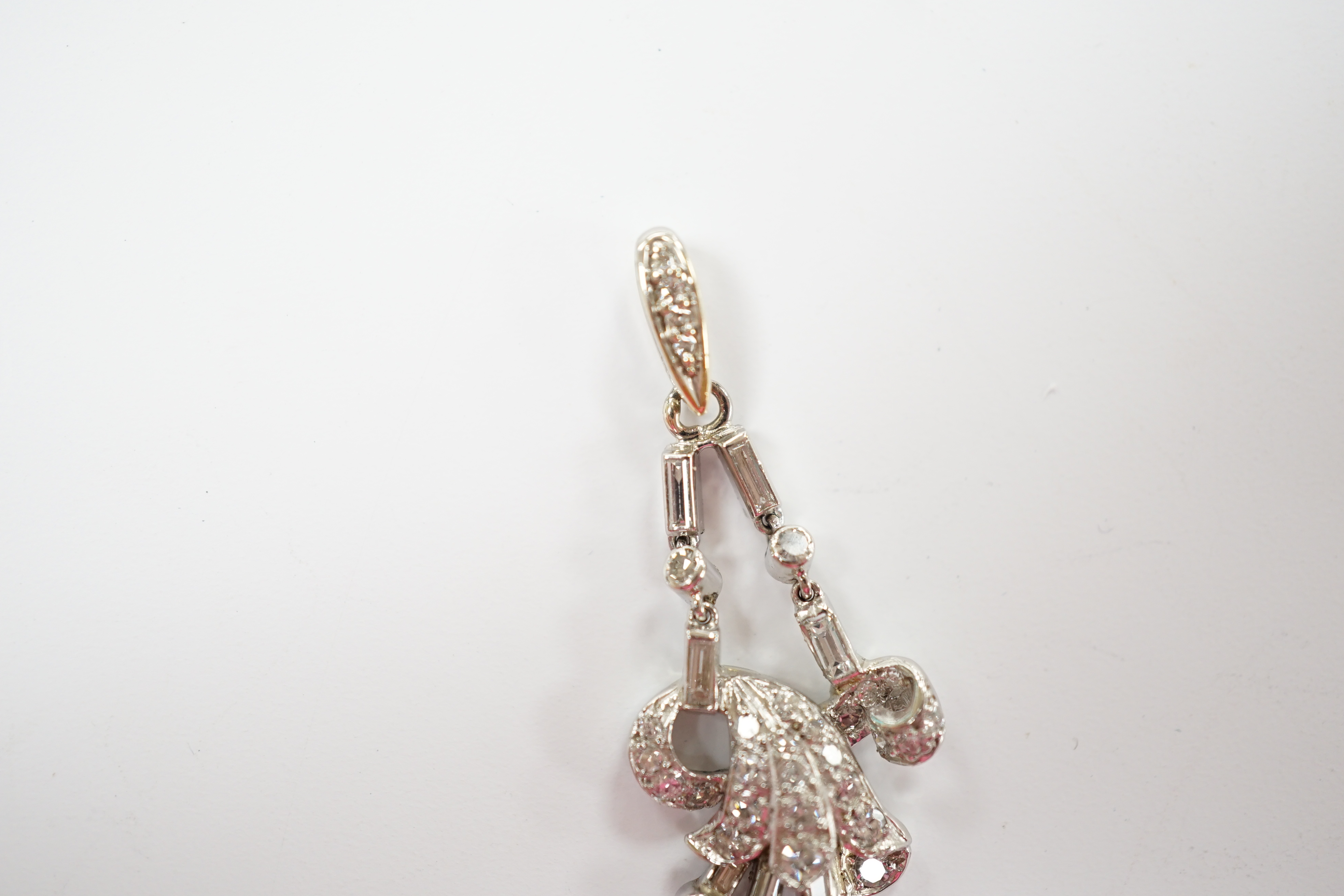 A white metal baguette and round cut diamond cluster set scroll pendant, overall 33mm, gross weight 3.6 grams.